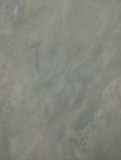 The image shows a close-up view of a textured surface, likely a wall or a concrete surface. The texture appears rough with visible pores and variations in color, ranging from light gray to a slightly darker, bluish-gray. There are subtle patterns and shadows that suggest a somewhat uneven surface. The lighting is diffused, creating a soft and muted overall impression. The image is devoid of any discernible objects, people, or actions, focusing solely on the abstract texture of the surface. The location in Hnivan, Ukraine, is not visually apparent from the image itself; it provides context for the origin of the photograph, suggesting the surface is found within that city.