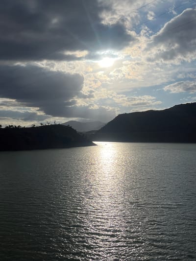The image shows a landscape with a body of water reflecting sunlight. On the left, there are cloudy skies with power lines visible. Adjacent to the sky is a dark silhouette of a mountain range. The water's surface reflects the light, creating a shimmering effect. While Tabaroucht, Morocco is mentioned, there is no visual confirmation of the location. No people or specific objects are identifiable. The scene primarily depicts a natural landscape with a play of light and shadow.