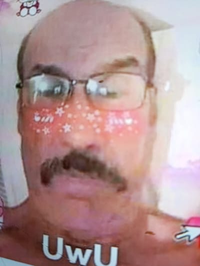 This media file is a close-up, slightly distorted image of a person's face. The individual appears to be a man with a receding hairline, wearing glasses and a mustache. His cheeks are adorned with pink blush and small white star-shaped stickers, giving him a whimsical or playful appearance. The background is blurred and light-colored, with hints of other elements that are difficult to discern.

The lighting in the image is bright, suggesting it was taken in a well-lit environment, possibly indoors with artificial lighting or near a window. There are no clear indicators of the time of day or weather conditions. The overall mood conveyed by the image is lighthearted and perhaps even humorous, due to the playful adornments on the face.

Visible text in the image includes "UwU" in large, white, block letters across the lower part of the frame, below the person's chin. There also appears to be a cartoonish, light-pink character with round ears and a smiling face at the top left of the image, and a white computer cursor with a pink arrowhead at the bottom right.

Given the provided location context of Krasivka, Ukraine, this image might be a screenshot from a video call, a social media post, or a digital photograph taken within that area. The combination of the person's features, the digital adornments, and the text creates a unique and somewhat surreal portrait.