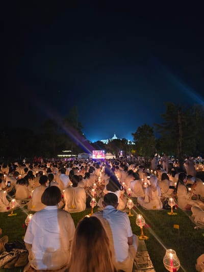 People are sitting on grass holding candles with a large building in the background. The location is Borobudur, Indonesia.