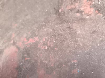 The image shows a close-up, abstract view of a textured, speckled surface. The predominant colors are various shades of grey and dusty pink, with small flecks of white and a few hints of blue. The surface appears to be slightly worn and possibly outdoors, with hints of dust and imperfections. There are no discernible people, animals, or specific objects that can be identified. The image provides no information about its location in Краснадворскі сельскі Савет, Belarus.