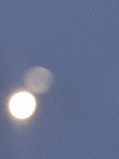 The image shows a bright, round object, likely the moon or sun, partially obscured by a hazy, cloud-like formation. The background is a textured, pale blue-gray sky. The object is positioned in the lower left quadrant of the image. The scene appears to be an outdoor environment under a somewhat overcast sky. No specific location within Ganderkesee, Germany can be identified from the visual information provided.