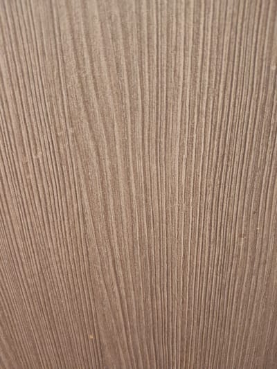 The image shows a close-up, abstract view of a textured surface. The texture consists of numerous fine, parallel vertical lines that appear to be either carved or naturally occurring in the material. The color of the surface is a muted, light brown or beige. There are no discernible objects, people, or environmental elements visible that would indicate a specific location within the city of Малое Верево, Russia, or any other location. The image is a detail shot focusing solely on the textural pattern of an unknown material.