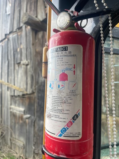 The image depicts a red MFZ/ABC1 dry powder fire extinguisher. The label on the extinguisher includes instructions for use (aim at the flame, press down the handle), as well as information about the types of fires it is suitable for (A, B, C, and E). Text details operation and environmental temperature ranges, fire extinguishing grade, composition of the extinguishing agent and driving gas, and working pressure. It also indicates that the product is manufactured according to GB4351.1-2005. The extinguisher is positioned in front of a wooden structure. The location is not evident.