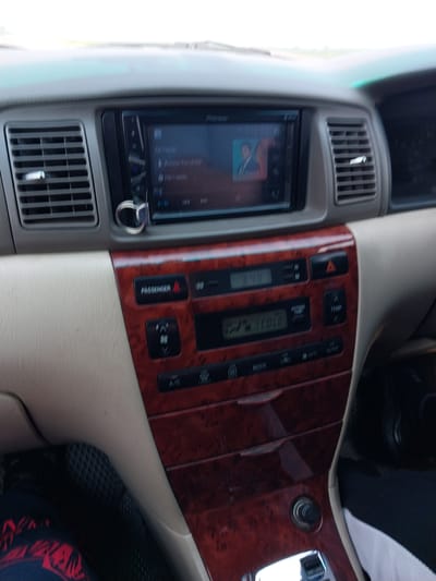An interior view of a car's dashboard displays a central infotainment system, climate control, and other vehicle functions. The infotainment screen, a Pioneer model, shows music playback information and album art. Below it, a digital display shows "3:48" and climate control settings, including "OUTSIDE TEMP" and "COLD". Various buttons and knobs control functions like "PASSENGER", temperature adjustment ("TEMP"), hazard lights, and A/C. The dashboard is accented with a wood-grain trim. The image likely depicts the car's interior while parked or driving in Sychevka, Russia, though no specific indicators of the city are present.