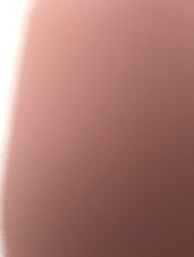 The image depicts an abstract composition of color and light, located in the city of Qanlikul, Uzbekistan. It features a dominant reddish-brown field with a fine, uniform grain texture across most of the frame. On the far left, a significant vertical area of intense white light extends from top to bottom, indicating an overexposed or highly illuminated region. No identifiable people, specific subjects, objects, actions, interactions, or discernible environmental features are present within the visual frame.