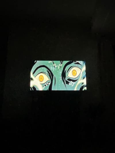 The image shows two pairs of wide, stylized eyes. The eyes are rendered in shades of green and black, with striking yellow irises. They are surrounded by what appears to be water or a similar liquid, with visible bubbles and motion lines. The eyes are positioned vertically, one pair above the other, in the center of a predominantly black background. The scene is illuminated, possibly from a screen or light source behind the image.