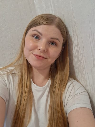 A woman with long, blonde hair is lying down, possibly on a bed or sofa. She is wearing a white t-shirt. The background appears to be a wall with a textured pattern. There is no indication of a location in the city of Ozyorny, Russia.