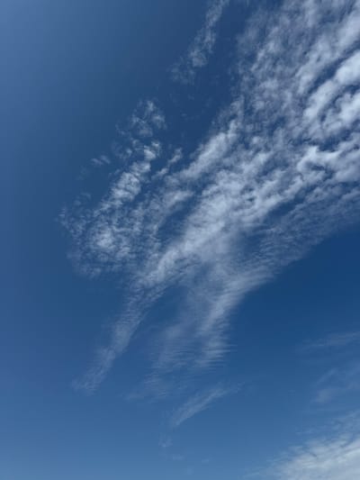 The image captures a vast expanse of clear blue sky with scattered white, wispy clouds. The clouds are thin and appear to be cirrus clouds, stretched across the sky in feathery streaks and patches. The lighting suggests it is daytime, with no visible sun or other celestial bodies. The composition focuses solely on the sky, with no ground features or any indication of a specific location within the city of Kalngale, Latvia. There are no people, subjects, objects, or actions depicted in the scene. The environment is exclusively the sky.