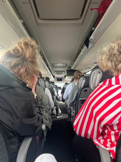 The image shows the interior of a TGV train, likely between seats due to the close proximity of passengers. The location is Bourgoin-Jallieu, France. Passengers are seated. Personal items such as bags and a red backpack are in the overhead compartment.