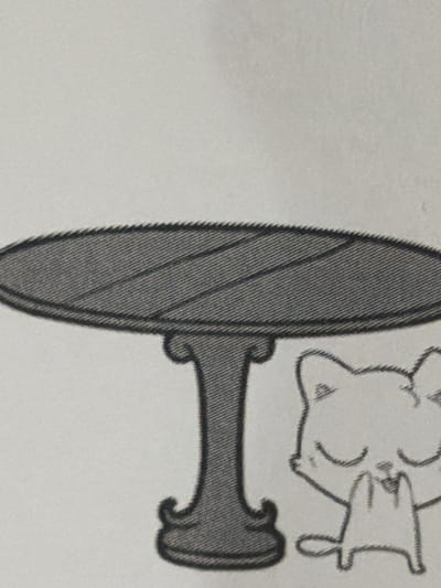 The image depicts a black and white line drawing of a table and a cartoon cat. The table is round with a textured surface and a pedestal base that flares out at the bottom. To the right of the table is a cartoon cat with its eyes closed and paws clasped in front of its chest. The cat has pointed ears and a simple body. The drawing is on a light-colored background, likely paper. There is no indication of any specific location in the city of Arcahueja, Spain, within the image.
