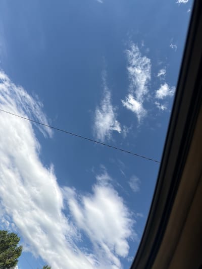 A view of a blue sky with scattered clouds through a car window. A power line runs diagonally across the sky. Some trees are visible in the lower right corner. The location in the city of Dimitrov, Armenia, is not verifiable from the image.