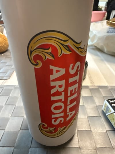 The image shows a white can with a red "Stella Artois" logo. The can is lying on a table with a light grey tiled surface. A small box is visible in the background. The image does not contain enough information to determine if it was taken in Petkovo, Bulgaria.