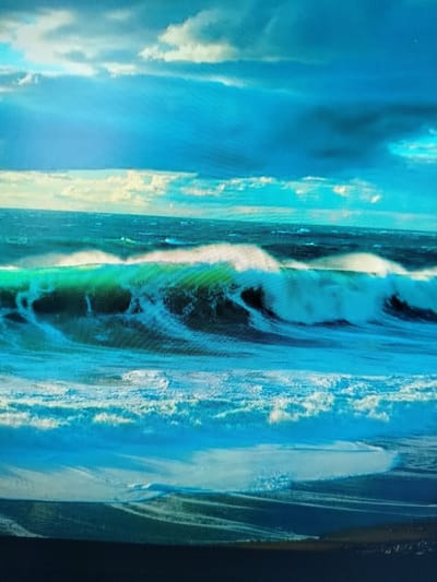 The image is a photograph of a turbulent ocean scene under a cloudy sky. The waves are large and crashing, with white foam at their crests. The water is a deep blue and green, with streaks of white from the waves. The sky is a mix of blue and dark gray clouds, with some lighter areas suggesting sunlight breaking through. The overall impression is one of power and wildness. The image does not contain any discernible landmarks or elements that would suggest it is located in Yashkino, Russia.