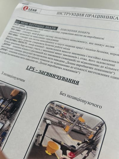 This media file is a photograph of a document with text and an image. The document appears to be an instruction manual or a guide for workers, with the title "ІНСТРУКЦІЯ ПРАЦІВНИКА" (Worker's Instruction) prominently displayed in Ukrainian.
The text on the left side of the document discusses various standards such as IATF 16949, ISO 14001, and ISO 45001, relating to quality management, environmental management, and occupational health and safety. It also outlines a "ПОЛІТИКА ЯКОСТІ" (Quality Policy) and mentions "RPPM" and "IPPM" as indicators. The word "LPS" is also visible, followed by what appears to be a process name "загвинчування" (screwing).
On the right side of the document, there is a close-up photograph of industrial equipment, likely on an assembly line. The equipment consists of various metal components, machinery, and tools. Bright yellow elements are visible, possibly indicating safety features or labels. The setting appears to be a factory or a production facility.
The overall impression is a professional document detailing operational procedures and standards within an industrial context. The image of the machinery serves as a visual aid or example related to the instructions provided. There are no people visible in the photograph. The lighting in the photograph of the document suggests it is taken indoors, possibly in an office or workshop. The image of the machinery appears to be well-lit, consistent with a factory environment.