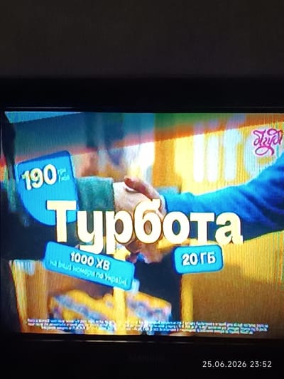 The image is a photograph of a television screen displaying an advertisement. The advertisement features a large white text that reads "Турбоота". To the left of this text, there is a blue badge with the number "190" in yellow. Below the main text, there are two smaller blue badges. The left one displays "1000 ХВ" and below it, in smaller text, "на будь-який номер по Україні". The right blue badge displays "20 ГБ". At the top right corner of the screen, there is a stylized pink logo. The background of the advertisement is a blurred yellow and orange pattern. A timestamp at the bottom right of the image indicates "25.06.2026 23:52". The image itself is a low-quality photograph of a screen, with some visual distortions and noise. There is no identifiable location within the city of Bolhrad, Ukraine, as the image depicts a commercial advertisement on a screen, not an outdoor scene.