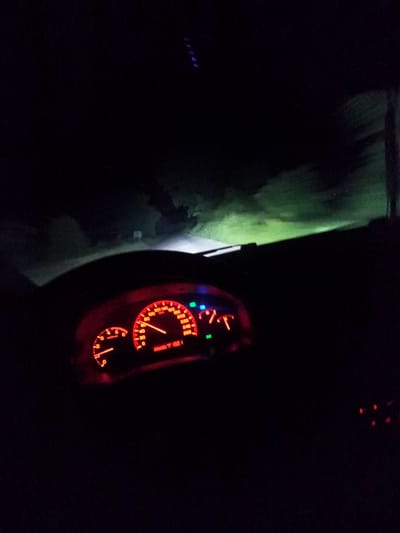 The image shows a car interior at night, viewed from the driver's perspective. The dashboard is illuminated, displaying red gauges, including the speedometer which indicates a speed around 60 mph. The tachometer is also visible. Through the windshield, a dark, blurry scene suggests movement along a road possibly located in Padarsko, Bulgaria. Due to the lack of details, it is impossible to identify any specific landmarks or other objects in the surrounding environment, making a forensic analysis of its location incomplete.