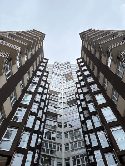 The image shows a worm's-eye view of two modern apartment buildings in La Coruña, Spain, with a gray, overcast sky visible between them. The buildings have a similar design, with dark brown sections contrasted by white or light-colored sections with many windows. Balconies are visible along the edges of the buildings. The image appears to be vertically mirrored.