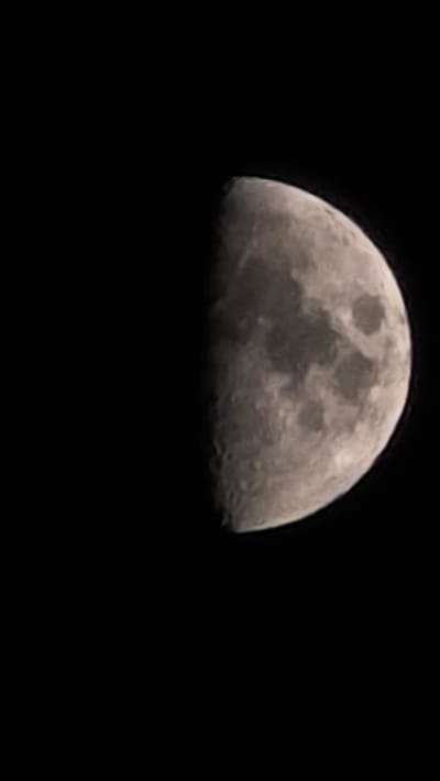 A photograph of the moon, approximately half illuminated, against a black sky. The moon's surface features are visible, including craters and darker maria. The image is oriented vertically, with the moon occupying the right side. The left side of the image is completely black. There is no indication of the city of Oyskhara, Russia, or any other environmental or human elements within the frame.