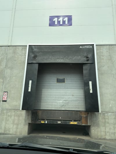 The image shows a loading dock with the number "111" on the adjacent wall. The loading dock door has the word "ALUTECH" printed vertically on its side. The loading dock is surrounded by concrete walls. The location is a building in Sluchainyi, Russia.