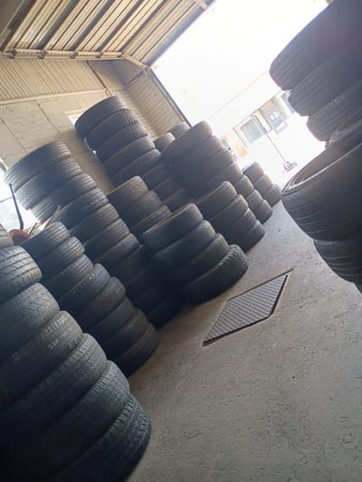 The image depicts a storage area filled with stacks of tires. The tires are piled up against a concrete wall. A metal grate is visible on the wall near the tires. The location is most likely a tire shop or a storage facility in the city of Clarksville, United States of America.