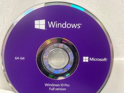 The image shows a close-up of a purple CD or DVD labeled "Windows 10 Pro Full version" and "Microsoft". The Windows logo is also visible. The disc has a silver ring around the edge and a holographic pattern in the center. The background is a textured, off-white surface. There is no indication of the city of Mülheim an der Ruhr, Germany.