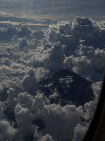 The image depicts an aerial view of a landscape dominated by dense cloud cover, with a dark, triangular shape, potentially a mountain peak, visible amidst the clouds. The overall scene is captured from an elevated perspective, seemingly from an aircraft window. No people or specific objects are discernible beyond the clouds and the ambiguous mountain shape. The context of Taoyuan City, Taiwan, is provided but not explicitly visible within the image.