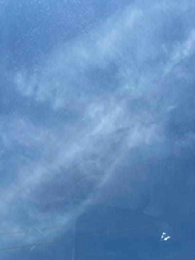 The image shows a blue sky with streaky cirrus clouds. The image is taken through a window, as evidenced by reflections and a linear distortion along the right edge. The location in the city of Kueda, Russia, is unknown and cannot be determined from the visual information.