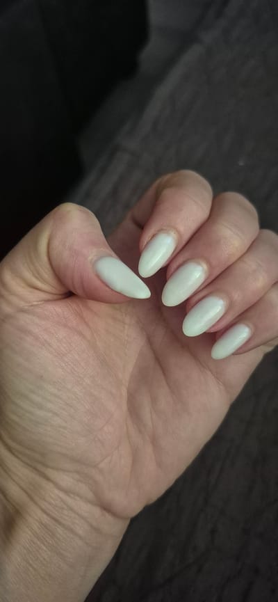 The media file is a close-up, top-down view of a person's hand with neatly painted nails. The nails are almond-shaped and have a light, pearlescent white polish. The hand is resting on a dark, textured surface, possibly a wooden table or a fabric. The lighting is soft, casting gentle shadows and highlighting the sheen of the nail polish and the texture of the skin.
The image focuses entirely on the hand and nails, suggesting the subject matter is related to personal grooming or aesthetics. There is no visible text. The background is dark and out of focus, drawing all attention to the well-manicured hand. The overall impression is one of neatness and subtle elegance. The location context provided, Metsamor, Armenia, does not offer specific visual cues within the image itself.
