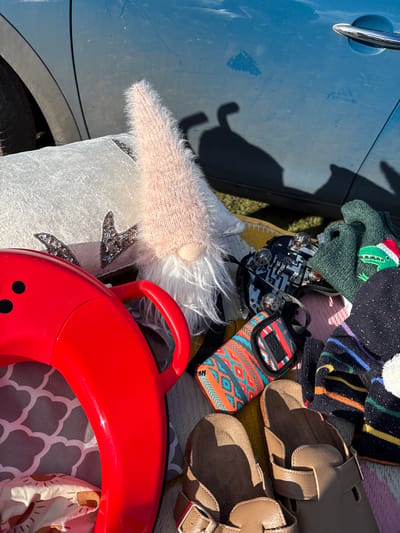 The image shows various objects placed on a yellow striped mat next to the blue car. There's a light pink gnome, some hats, a pair of brown baby shoes, a black taillight and a red toy.
The location is not specified, though the prompt stated it was in the city of Chirk, United Kingdom.