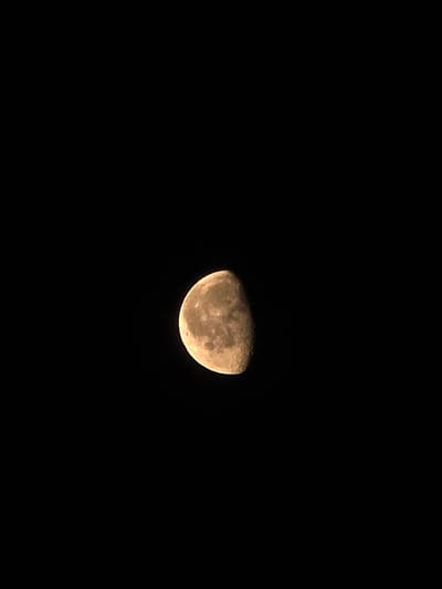 The image is a close-up of the moon against a black sky. The moon is in its gibbous phase, with approximately two-thirds of it illuminated. The surface of the moon shows craters and variations in shading, indicating the presence of mountains and valleys. The color of the moon appears to be a yellowish-brown, possibly due to atmospheric conditions or the camera's white balance. The background is entirely black, devoid of any stars or other celestial objects, suggesting that the exposure was optimized for the moon itself. The image appears to be a photograph taken from Earth, focusing on the lunar surface. There is no indication of any specific location within a city, such as Икское Устье, Russia, or any people or actions.