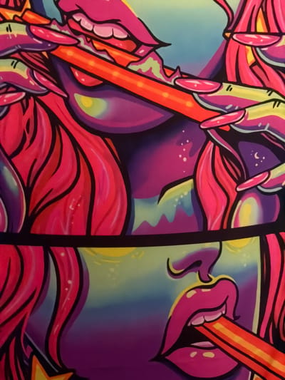 A close-up view reveals a section of a vibrant, highly stylized graphic artwork, located in Saint-Leu-la-Forêt, France. The illustration employs a neon color palette with bold black outlines and depicts fragmented human-like features. In the upper half, multiple instances of pink lips with visible white teeth are depicted, one appearing to bite. A slender hand with long, pink-nailed fingers is centrally positioned, grasping an orange and yellow striped cylindrical object, approximately 1.5 cm in width, extending diagonally. Below a distinct horizontal black band, a third set of pink lips holds an identical striped object. Stylized, flowing hair rendered in bright magenta and pink frames these elements. The background within the artwork transitions from a light blue-green at the top to a dark purple, featuring subtle glowing highlights and scattered white specks.