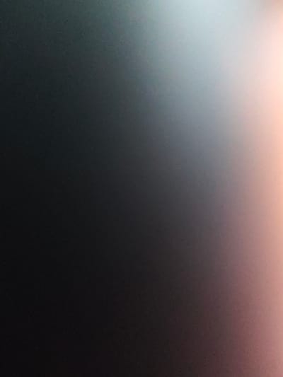 This media file is an abstract, out-of-focus image with a gradient of colors. The left side of the image is dark, transitioning through shades of gray and blue in the middle, and ending with a bright, peachy-pink hue on the right. The texture appears to be grainy or slightly speckled. There are no discernible subjects, objects, or scenes. The image does not depict any activity or event. There is no visible text. Due to the abstract nature of the image, details like time of day, weather, location cues, or emotions are not applicable. The provided location context of Lügde, Germany, does not offer any visual clues within the image itself.
