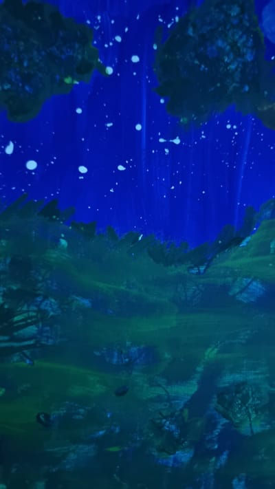 This is an abstract painting with a dark blue sky speckled with white dots, possibly representing stars. The lower portion of the painting features dark green and blue abstract shapes that suggest foliage or a landscape. The painting does not depict any recognizable location in Heidenheim an der Brenz, Germany, nor does it contain any people, subjects, objects, or actions. It is a non-representational artwork.