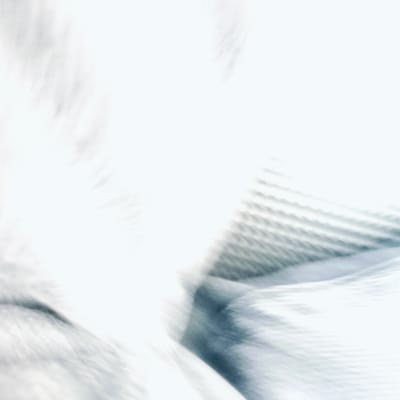 The media file displays a highly abstract image characterized by bright white and light grey tones, with subtle hints of bluish-grey. The composition is dominated by soft focus, pronounced motion blur, and diffused lighting, making it difficult to discern specific subjects or a clear scene.

On the left and extending into the foreground, there are blurry, undulating shapes with a soft, possibly fluffy or feathery texture. These forms are rendered in varying shades of white and light grey, with darker grey areas suggesting folds or deeper shadows within a soft material, possibly fur or plush fabric. The extreme diffusion of these shapes creates a sense of ethereal movement.

Towards the right and upper right of the image, a more defined, yet still soft, repetitive pattern is visible. This pattern consists of parallel diagonal lines or ridges, suggesting a ribbed, woven, or meshed texture. This structured element provides a contrast to the more amorphous forms on the left, though it too appears softly blurred, implying a textured fabric or surface viewed through a hazy effect.

The overall impression is one of lightness, softness, and dynamic movement. The bright white areas are intensely luminous, suggesting strong illumination. No specific people, distinct objects, or discernible activities are depicted. The image is an abstract composition focusing on light, texture, and blur. No text is visible within the image. The provided location context cannot be visually confirmed from the abstract nature of the media.