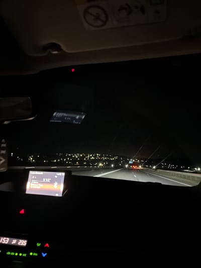 The image shows a night-time view from inside a vehicle on a highway. The dashboard displays information on a screen, with a digital clock showing "0:55" and other unreadable text. The road ahead is illuminated by headlights, and distant city lights are visible on the horizon. The sky is dark, and the interior of the car is dimly lit. There is a "VIP" label attached to the rearview mirror, suggesting the presence of a premium service or a personal designation. The image was taken in Ciocîlteni, Moldova, indicated by the metadata.