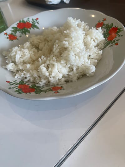 A white bowl with a floral pattern of orange and green flowers holds a mound of white rice. The bowl is positioned on a white surface, possibly a table, with a diagonal seam running through it. The lighting suggests an indoor setting, possibly a restaurant or home in Medan, Indonesia. No people or other objects are clearly visible.