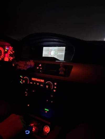 The image shows the interior of a car at night, with the dashboard illuminated. The infotainment screen is visible, displaying options like "Communication" and "Navigation". The climate control panel is also illuminated, showing a temperature of 24.0 degrees Celsius. A gauge cluster with red backlighting is visible in the lower left. The steering wheel and a person's hand are partially visible on the right. No specific location information pertaining to Rahovtsi, Bulgaria can be derived from the image.