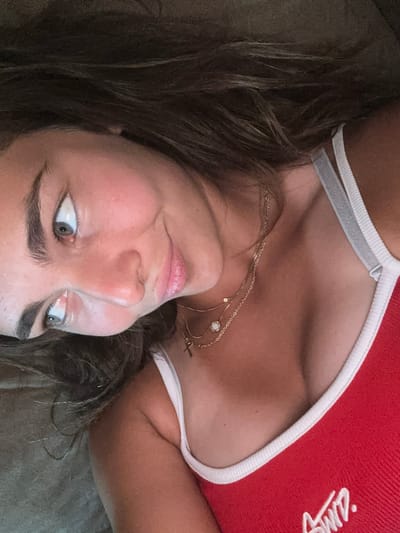 A woman lies on a grey surface. She wears a red tank top with white trim and a white logo. She has brown hair and blue eyes. She is wearing two gold necklaces.

There is no indication this picture was taken in Kashin, Bulgaria.