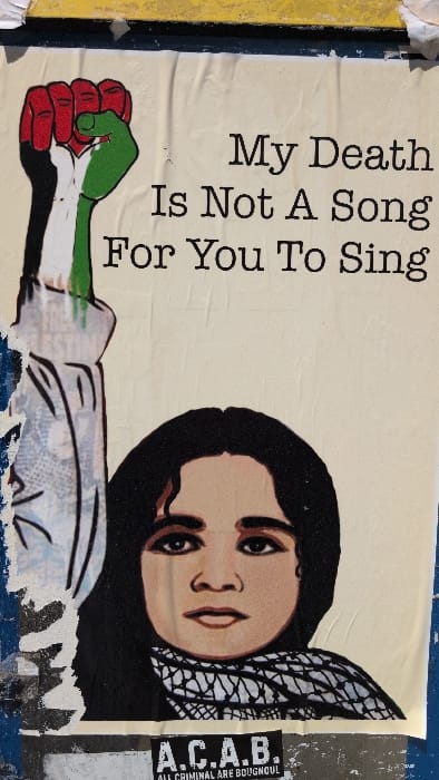 The image depicts a poster with a political message. The text reads "My Death Is Not A Song For You To Sing." The artwork includes a drawing of a woman wearing a black headscarf, and a fist is shown colored with the colors of the Palestinian flag. To the right of the woman is an "A.C.A.B." sticker, an acronym that stands for "All Cops Are Bastards," with the added message "ALL CRIMINAL ARE BOUGNOUL." The poster is adhered to a weathered surface.