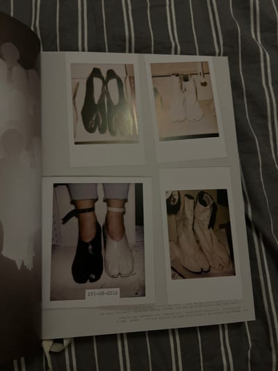 A page from a photography book showcases four images of split-toe shoes. Two top photos display pairs of white boots. The lower left image features black split-toe shoes. The bottom right photo presents a closer view of two feet wearing white and black split-toe shoes respectively, paired with ankle bracelets. A gray striped bedsheet is visible in the background. Text is visible on the book's right side.