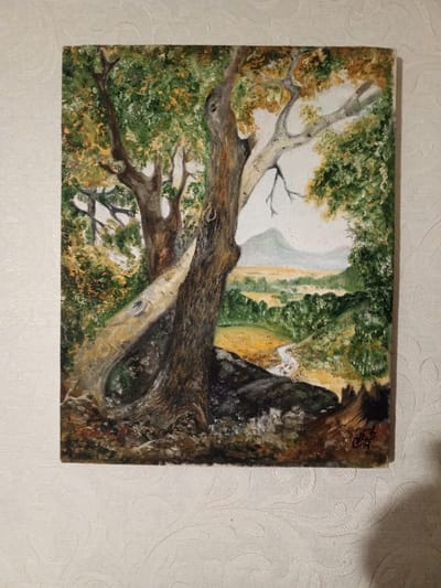 The image is a painting of a landscape. In the foreground, there are two large trees. The tree on the right has a thick, textured trunk and several branches. A lighter-colored, fallen log or branch rests diagonally against the trunk of the right tree. In the background, there is a valley with a winding stream or path, rolling hills, and a distant mountain under a hazy sky. The foliage of the trees is a mix of greens and yellows, suggesting autumn. The painting is signed in the lower right corner with initials that appear to be "А.Ф." or "А.В.". The painting is displayed on a textured, off-white wall. There is a shadow cast on the wall to the right of the painting. The location in the city of Belozernyi, Russia, is not discernible from the image itself.