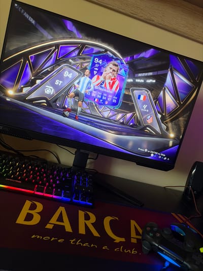 The image shows a gaming setup. A computer monitor displays a FIFA Ultimate Team card opening, featuring Antoine Griezmann. A keyboard with multi-colored backlighting sits on a mousepad branded with "BARCA more than a club." A gaming controller also lies on the mousepad. The location in Kozlovets, Bulgaria is not discernible from the image.