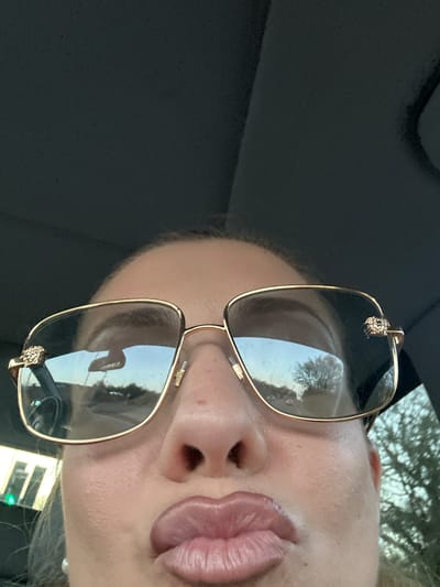 A close-up, rotated image shows a person wearing sunglasses, likely in a car. The reflection in the sunglasses suggests an outdoor setting with trees. The person is making a kissing face. The location, Basildon, United Kingdom, is not discernable from the image.