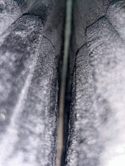 The image is a close-up, abstract shot of a dark, textured material with a seam running vertically down the center. The material appears to be soft, possibly fabric or foam, with a granular texture. Light is reflecting off the surface, creating numerous out-of-focus highlights that give the image a bokeh effect. The seam in the middle is slightly recessed, creating a shadow. The overall impression is one of depth and texture. The image is a detail of an unknown object, and no specific location in Lynnwood, Washington, USA can be identified from it.