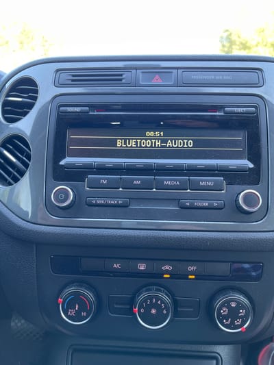 The image shows the interior of a car, specifically the dashboard with the infotainment system and climate controls. The infotainment screen displays "08:51" and "BLUETOOTH-AUDIO". Below the screen are buttons for "SOUND", "EJECT", and various media controls including "FM", "AM", "MEDIA", and "MENU". There is also a rotary dial with a power symbol and buttons for "SEEK/TRACK" and "FOLDER". To the right of these controls is another rotary dial, likely for volume or tuning.
Below the infotainment system are climate control buttons and knobs. The buttons include icons for defroster, recirculation, and "OFF". There are two prominent rotary knobs. The left knob controls temperature, with markings for "MAX A/C" and "HI", and a red and blue temperature indicator. The right knob controls fan speed and airflow direction, indicated by various fan and air direction icons.
The dashboard material appears to be dark plastic with textured surfaces. The ambient lighting suggests it is daytime, with sunlight filtering into the car, creating highlights and shadows. The overall impression is a standard car interior, common in modern vehicles. The image does not contain any information about the city of Pyrizhky, Ukraine.