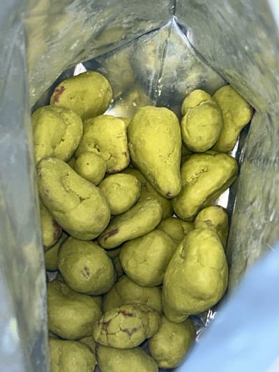 A close-up, indoor, overhead shot shows a pile of bright green, irregularly shaped candies, possibly coated peanuts or similar snacks, filling a silver bag. The candies are clustered together, with some overlapping and others partially obscured. The interior of the bag is visible, reflecting light. No people or activities are depicted. The scene is forensic and matter-of-fact, focusing solely on the visual elements of the objects within the bag. The location in Everett, United States of America, is not visually represented in the image and cannot be determined from the visual information provided.