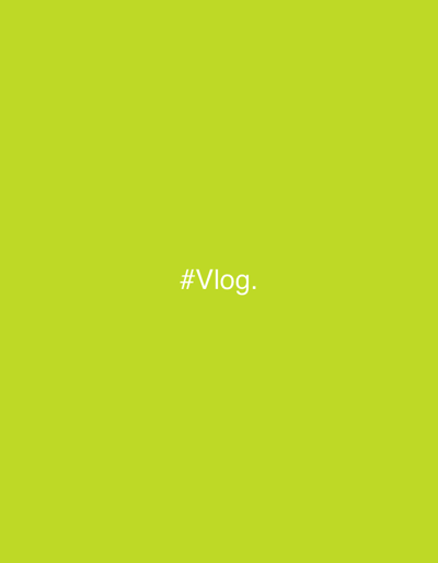 The image, associated with Kalyvia Thorikou Municipal Unit, Greece, displays a uniform chartreuse green background. Centered within the frame is the white text "#Vlog.", rendered in a sans-serif typeface. No human figures, discernible objects (other than the text), or specific environmental features are present. The scene is abstract, characterized solely by color and text.