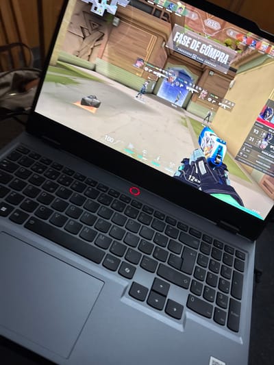 A laptop displays the game Valorant. The "Fase de Compra" (Buy Phase) is active with a 0:15 timer. Player health is at 100. The laptop features a standard QWERTY keyboard with black keys and a gray surrounding surface. A red circular power button is visible near the hinge. Game stats, including player scores and abilities, are shown on the top right of the screen.