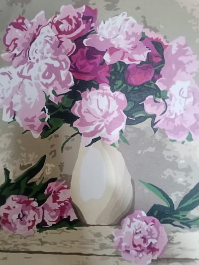 This is a painting of a bouquet of peonies in a vase. The peonies are in various shades of pink and magenta, with some white petals. The vase is a light cream color with subtle shading. The background is a neutral beige color with some abstract patterns. There are also a few fallen peonies and green leaves scattered around the base of the vase. The painting appears to be done in a style that resembles paint-by-numbers, with clear, defined color blocks. There is no information within the image or its provided crops that can indicate its location in the city of Yampil, Ukraine.